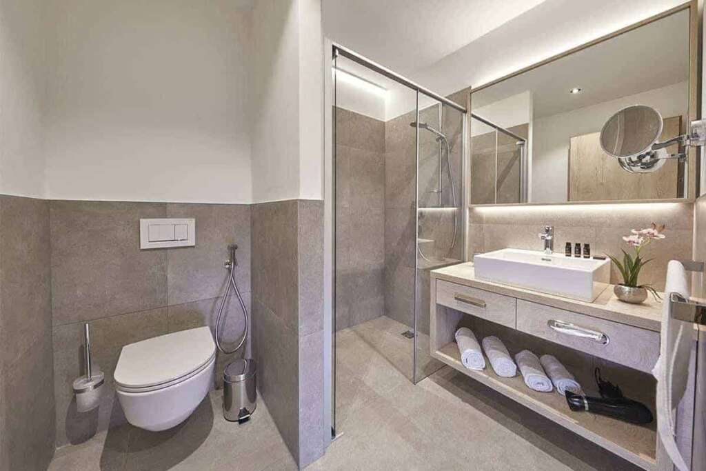 Modernes Badezimmer mit grauen Fliesen, Glasdusche, Waschtisch und gerollten Handtüchern