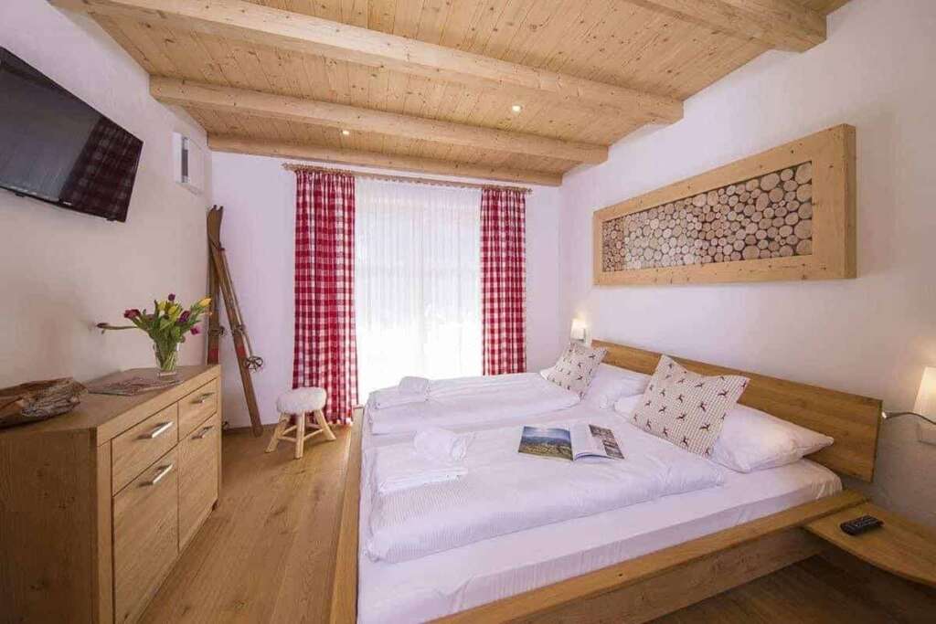 Doppelzimmer mit Holzbalkendecke, rot karierten Vorhängen, Holzbett und Tulpen auf der Kommode