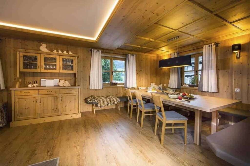 Holzgetäfelte Stube mit Kassettendecke, Anrichte, langem Esstisch und indirektem Licht