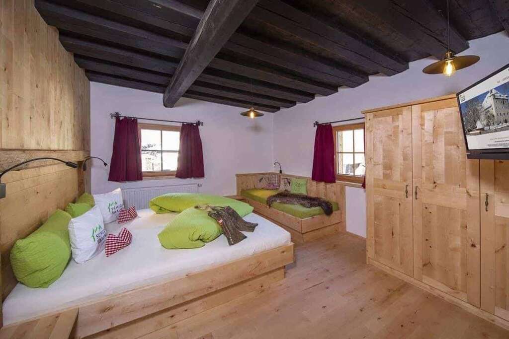 Schlafzimmer mit dunkler Balkendecke, Holzschrank, Doppelbett und Einzelbett mit grüner Bettwäsche