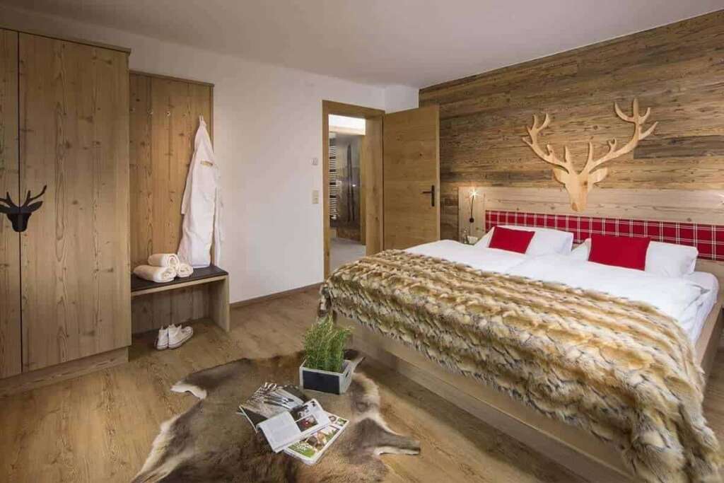 Schlafzimmer mit Altholzwand, Hirschkopf aus Holz, Felldecke, Fellteppich und Garderobe mit Bademantel