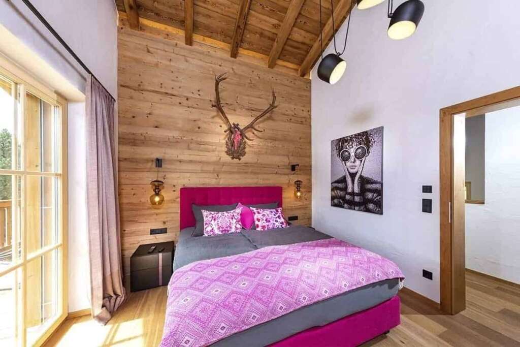 Schlafzimmer mit Holzwand, Geweih, pinkem Boxspringbett, großem Fenster und Kunstdruck