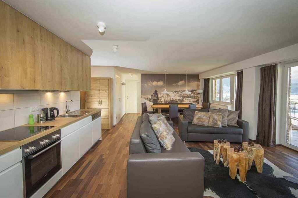 Offene Wohnküche mit grauen Ledersofas, Holzstumpf-Tischen, Esstisch und Bergfoto an der Wand