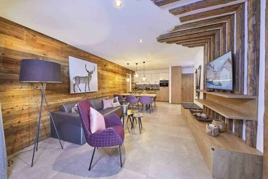 Offener Wohnbereich mit Altholzwand, Hirschbild, Sofa, violettem Sessel und Essbereich mit Küche