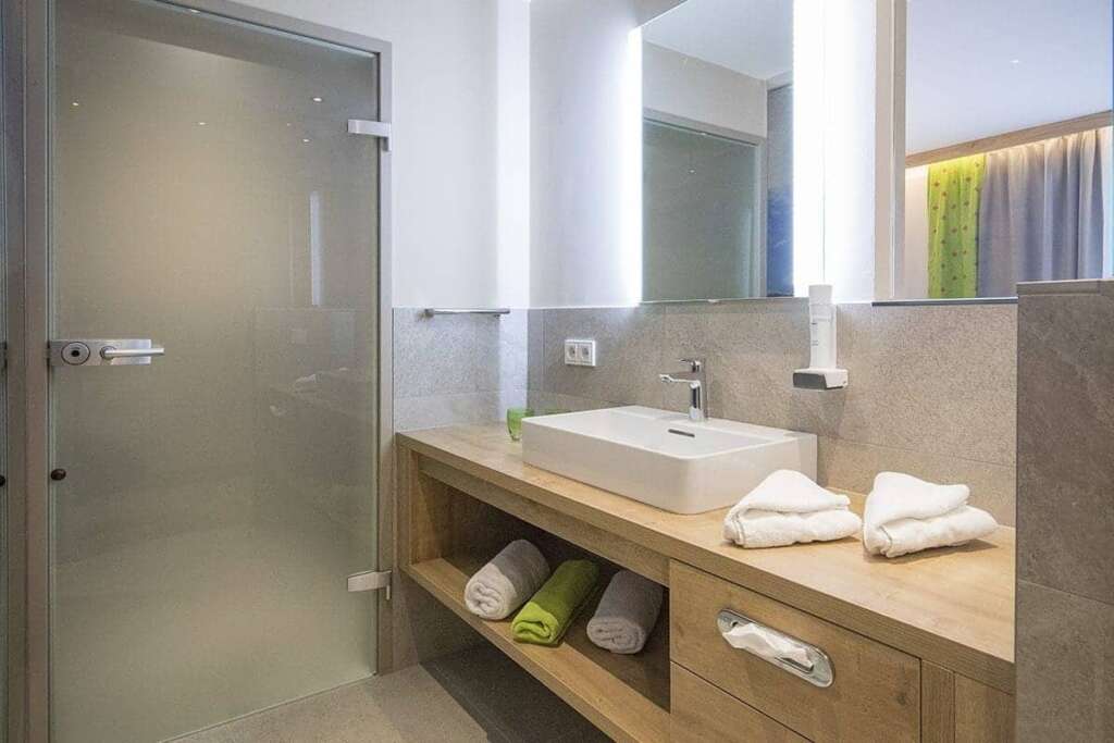 Badezimmer mit Milchglastür, Aufsatzwaschbecken, Holzwaschtisch und gerollten Handtüchern