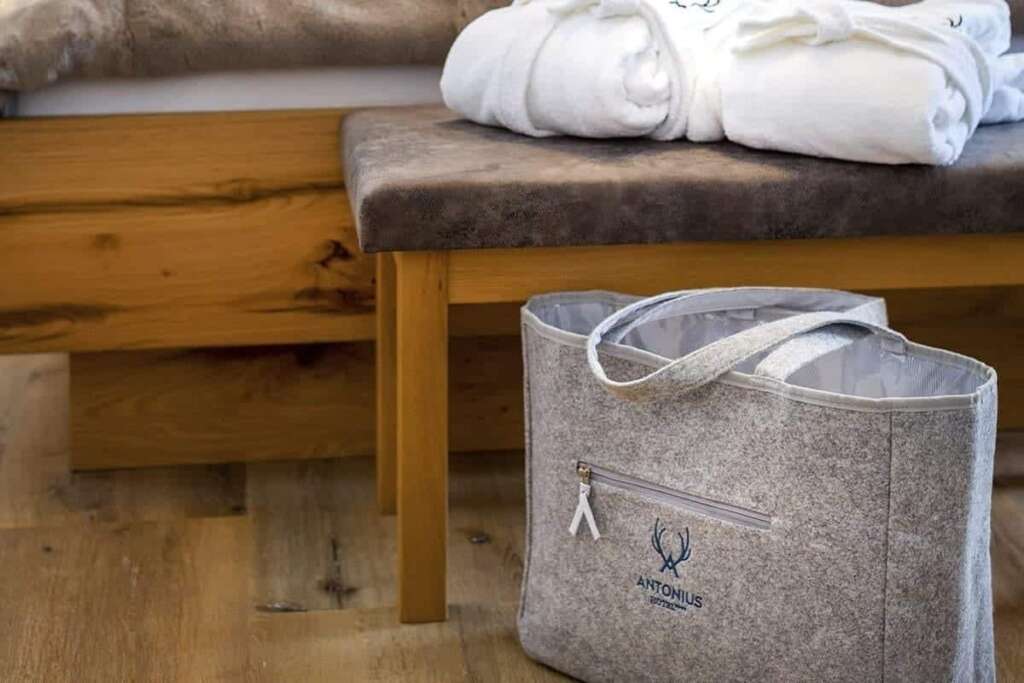 Graue Filztasche vor einer Holzbank mit gefalteten weißen Bademänteln auf Holzboden