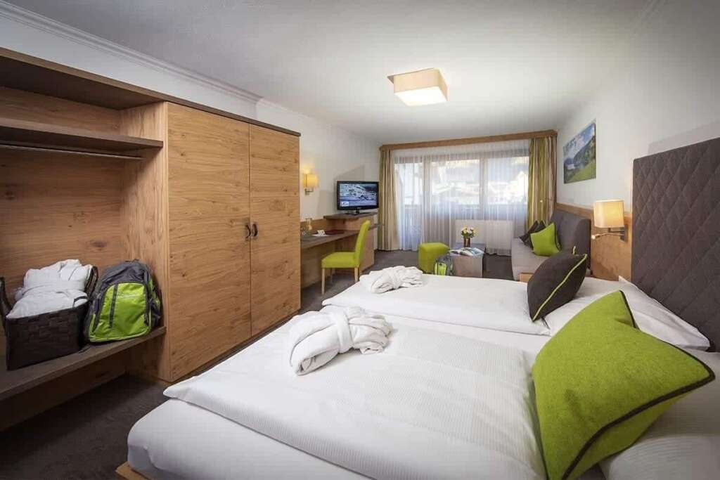 Doppelzimmer mit großem Holzschrank, grünen Kissen, Bademänteln auf dem Bett und Schreibtisch