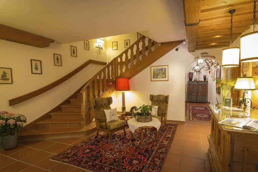 Traditionelle Eingangshalle mit Holzstiege, Ohrensesseln, Perserteppich, Rezeption und Bildern an der Wand