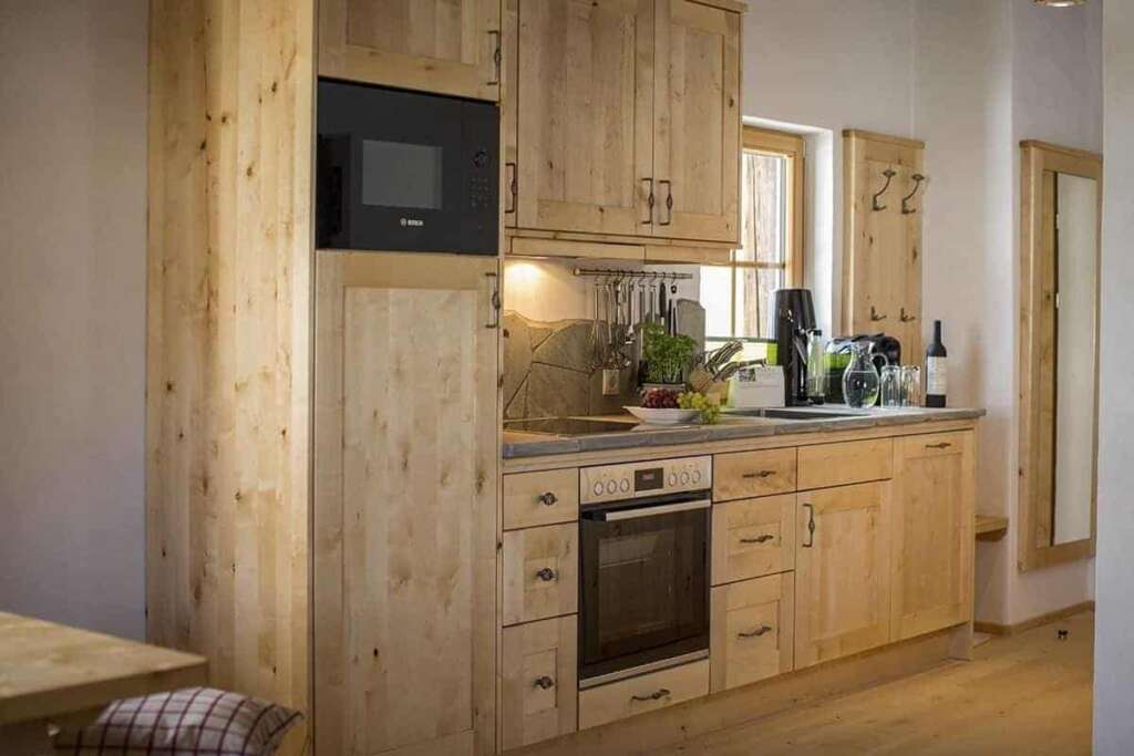 Küchenzeile aus hellem Holz mit Backofen, Mikrowelle, Utensilien und Fenster