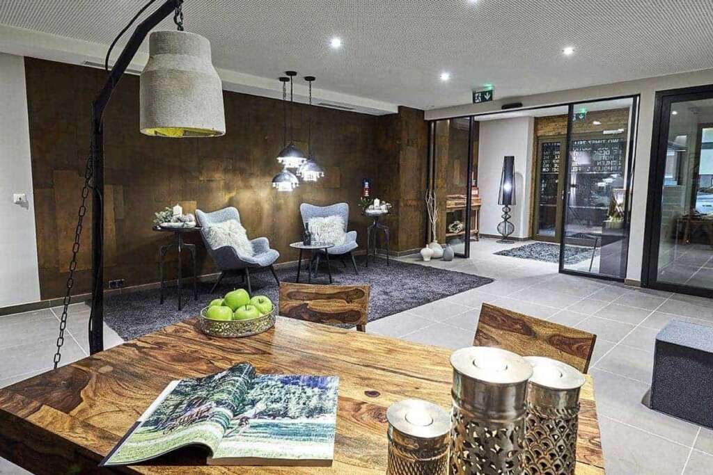 Hotellobby mit massivem Holztisch, Windlichtern, Äpfeln, Sesseln und Glastüren zum Eingang