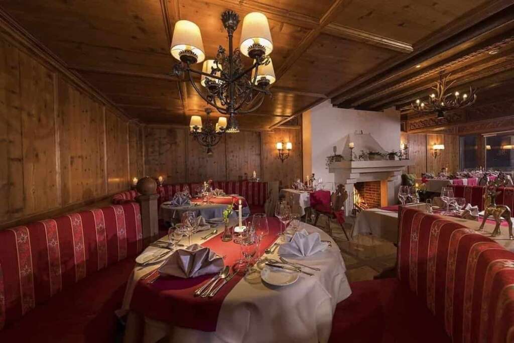 Holzgetäfeltes Restaurant mit Kronleuchtern, roten Polsterbänken, gedeckten Tischen und Kamin