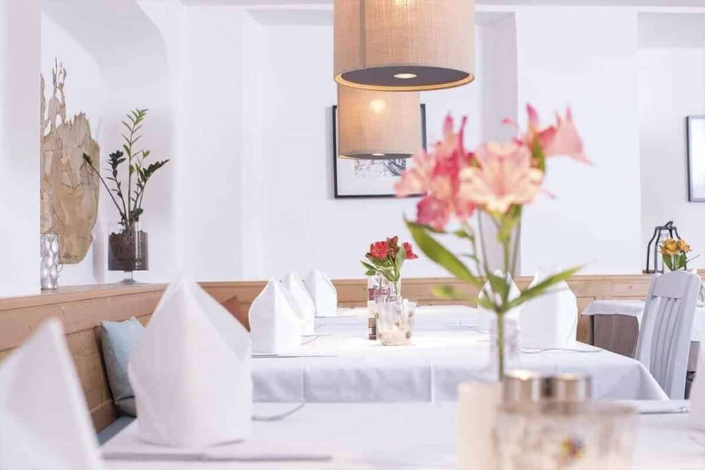 Weiß gedeckte Restauranttische mit gefalteten Servietten und Blumen, im Vordergrund unscharfe Lilien