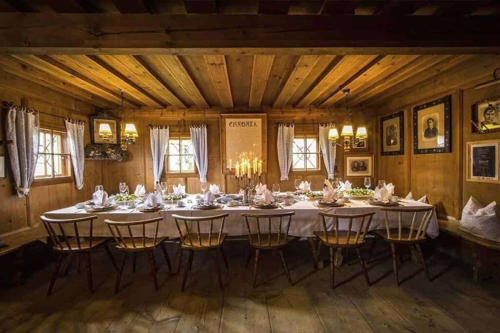 Alte Holzstube mit langer, festlich gedeckter Tafel, Kerzenleuchtern und gerahmten Bildern