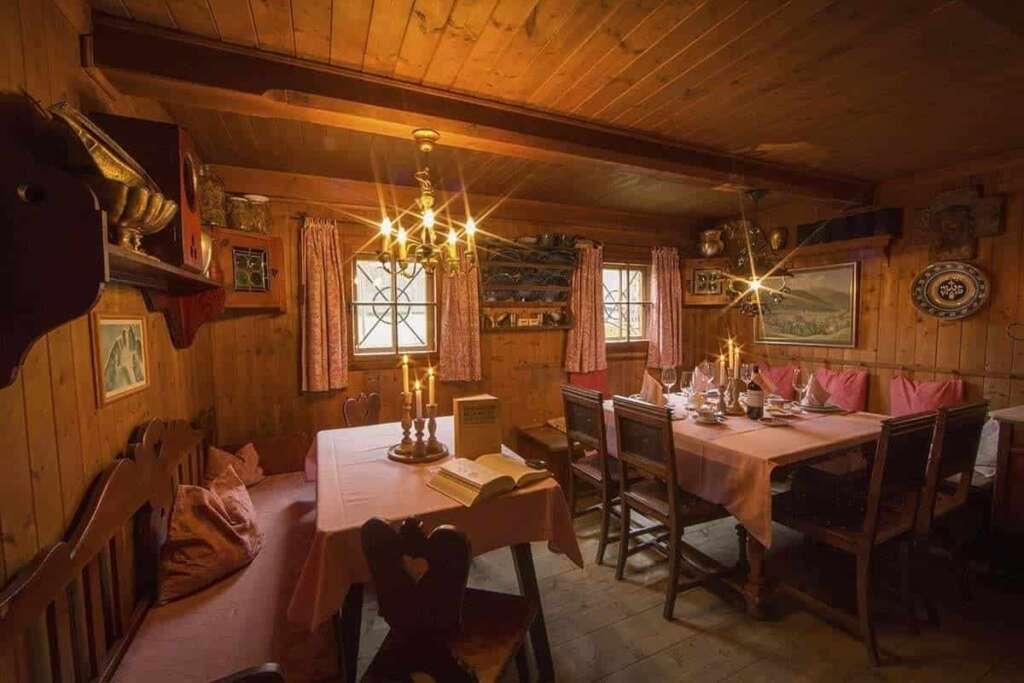 Holzstube mit rosa gedeckten Tischen, Kerzen, Kronleuchter, Eckbank und alten Bildern