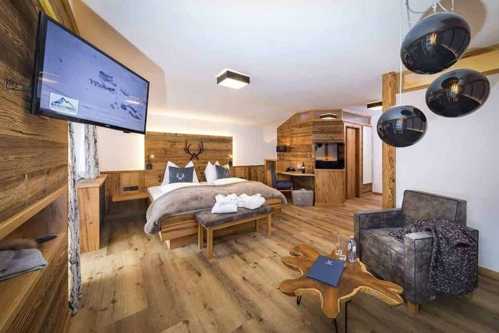 Hotelsuite mit Altholz, Doppelbett, Sessel, Wurzelholztisch, Kugelleuchten und Wandfernseher