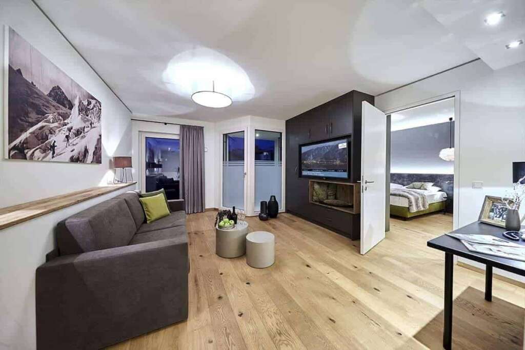 Suite mit Sofa, Beistelltischen, großem Bergfoto an der Wand und Blick ins Schlafzimmer