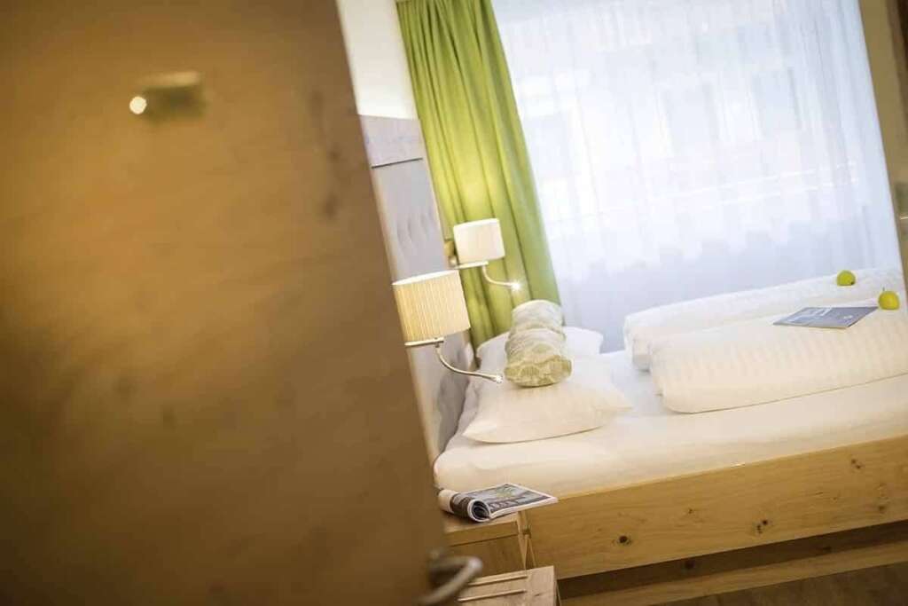 Blick durch eine halb geöffnete Tür auf ein Bett mit Leselampen und grünem Vorhang