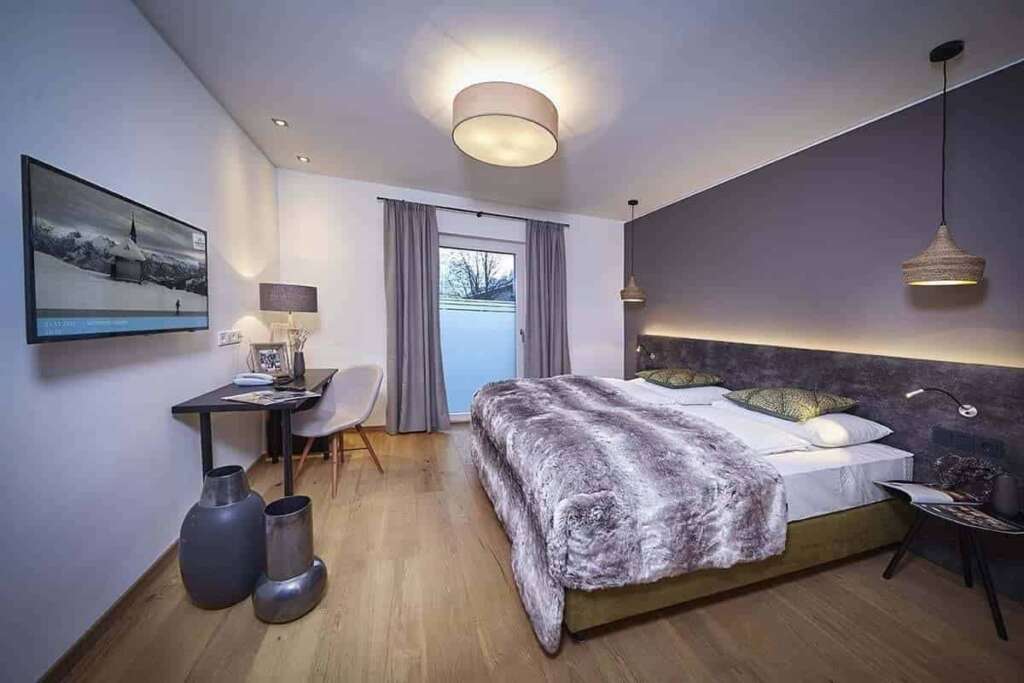 Modernes Hotelzimmer mit grauer Wand, Felldecke auf dem Bett, Pendelleuchte und Schreibtisch