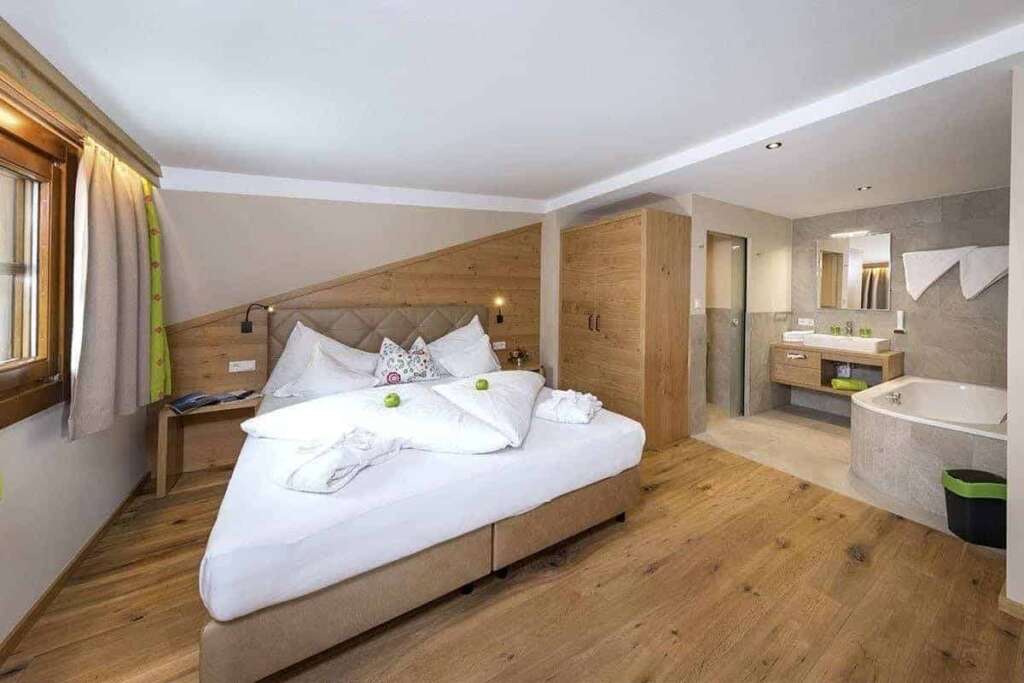 Hotelzimmer unter Dachschräge mit Doppelbett, Bademantel und offenem Bad mit Eckbadewanne