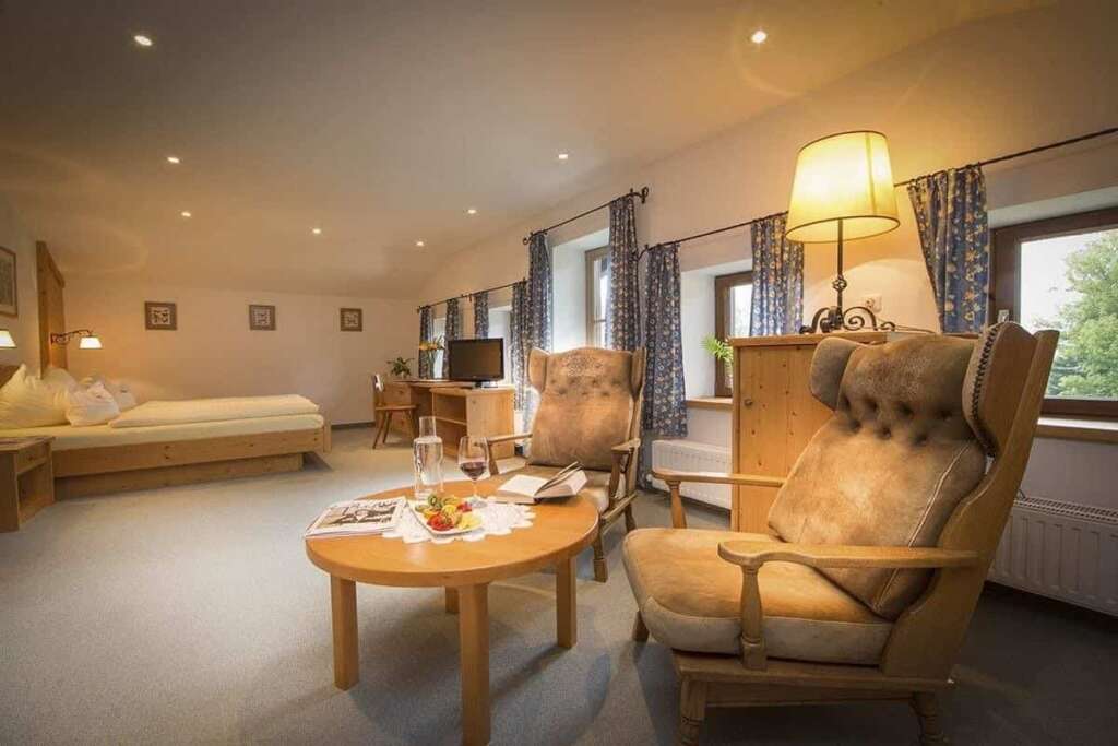 Hotelzimmer mit Ohrensesseln aus Leder, rundem Holztisch, Stehlampe und Bett im Hintergrund