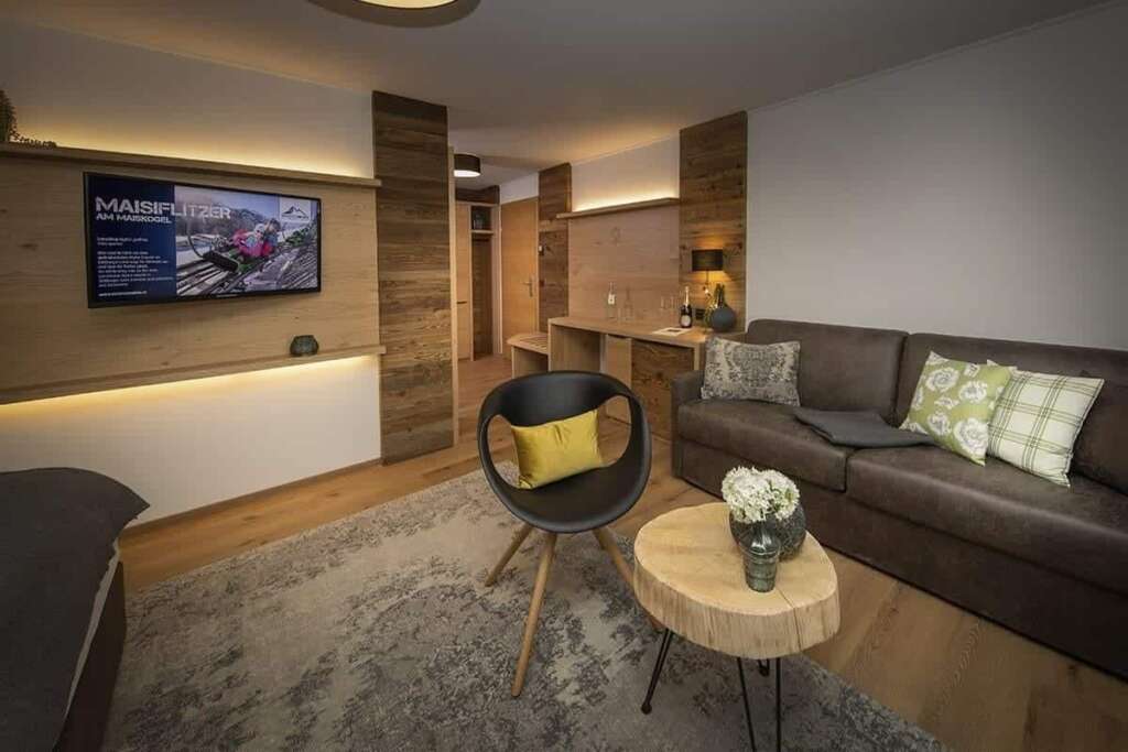 Hotelzimmer mit dunklem Sofa, Schalensessel, Baumscheibentisch, Altholzelementen und indirektem Licht