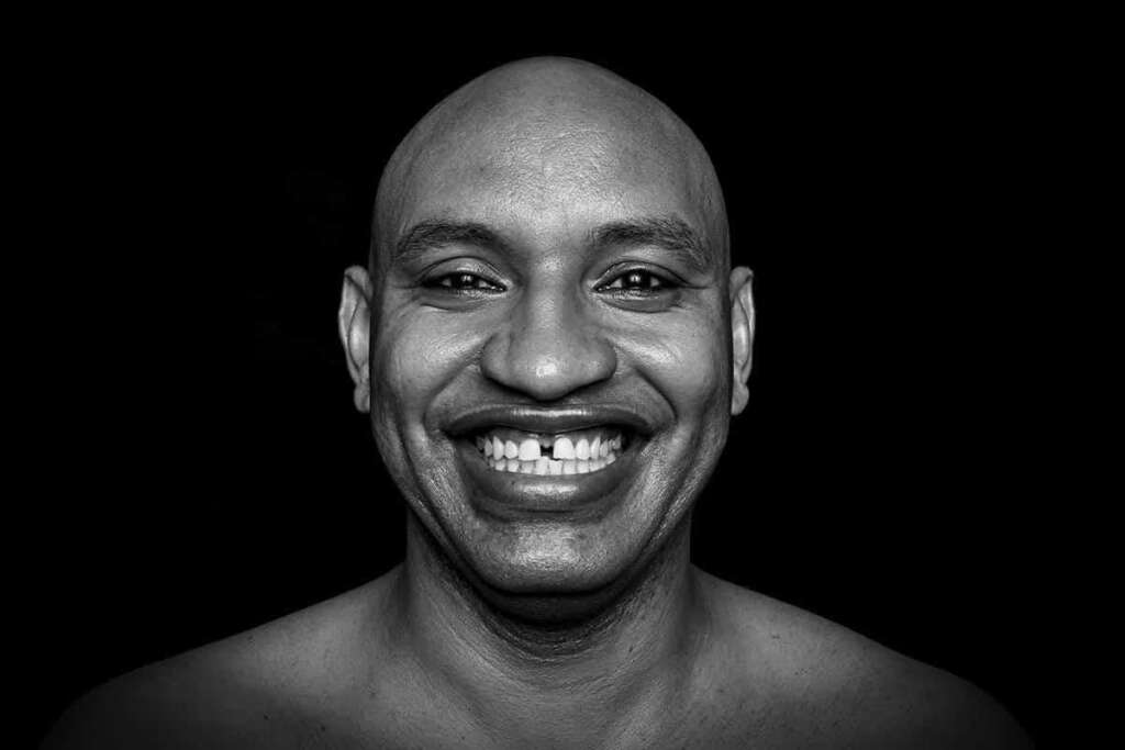 Schwarzweiß-Portrait eines lachenden Mannes vor dunklem Hintergrund